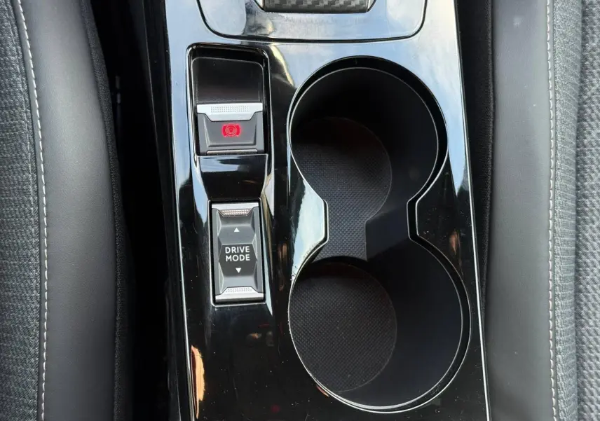 Gros plan sur la console centrale noire brillante avec bouton Drive Mode et frein à main électrique du Peugeot e-2008.