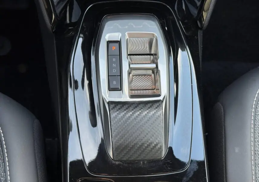Vue rapprochée de la console centrale noire brillante avec commandes de boîte auto et insert effet carbone du Peugeot e-2008.