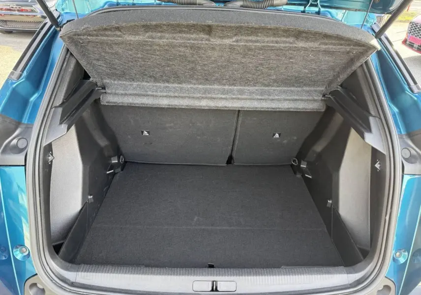 Coffre ouvert vu de l'arrière du Peugeot e-2008 bleu Obsession, montrant l'espace de rangement vide.