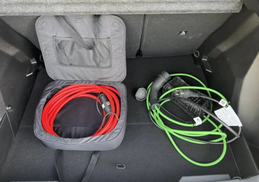 Coffre ouvert du Peugeot e-2008 2025 Bleu Obsession avec câbles de recharge électrique rouge et vert rangés.