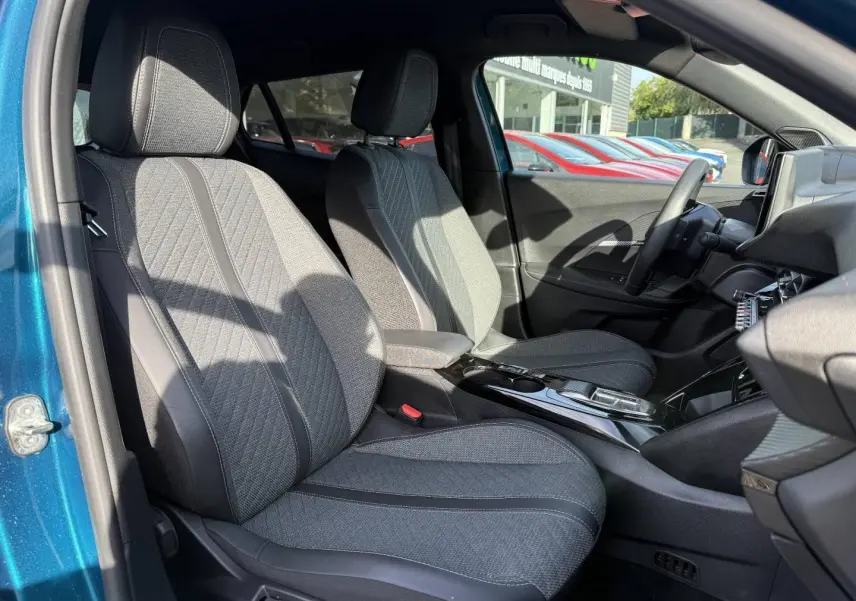 Vue intérieure côté gauche du Peugeot e-2008 2025 Bleu Obsession, montrant les sièges avant en tissu gris et la console centrale.