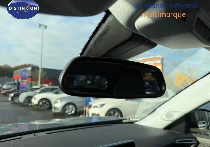 Vue intérieure centrée sur le rétroviseur intérieur d'une Peugeot 2008 gris Artense, avec vue floue sur des voitures blanches à l'extérieur.