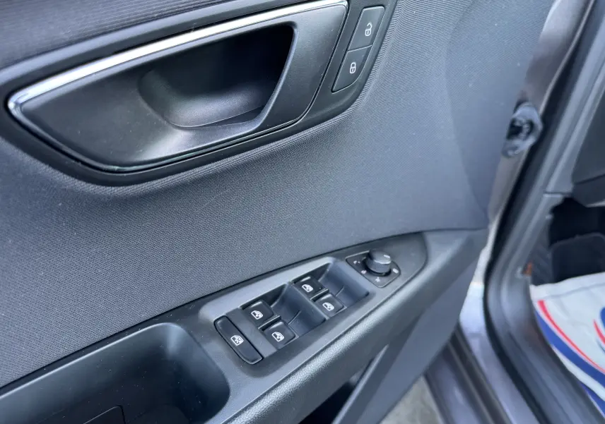 Vue rapprochée de la porte conducteur grise d'une SEAT LEON 2016, montrant les commandes des vitres et la poignée intérieure.