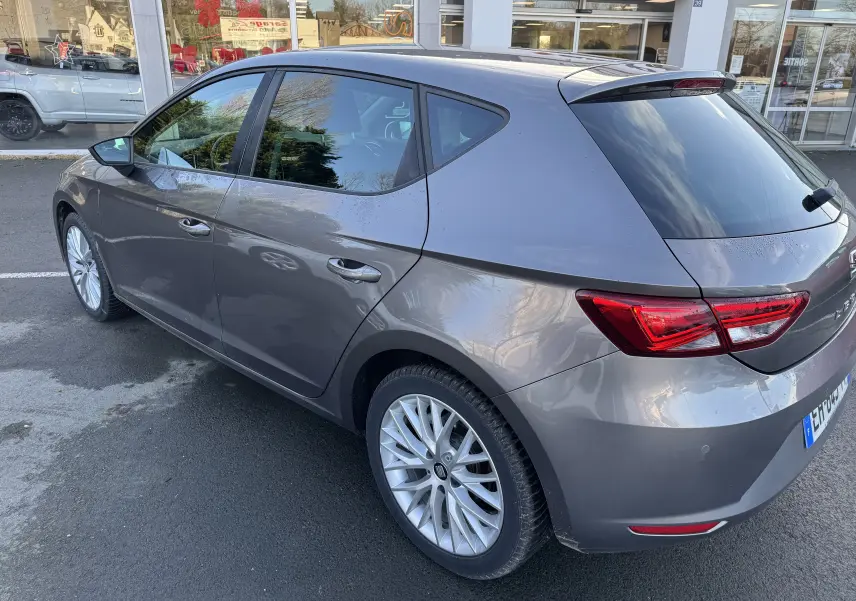 SEAT Leon gris vue 3/4 arrière côté gauche, mettant en valeur les feux arrière et les jantes alliage.