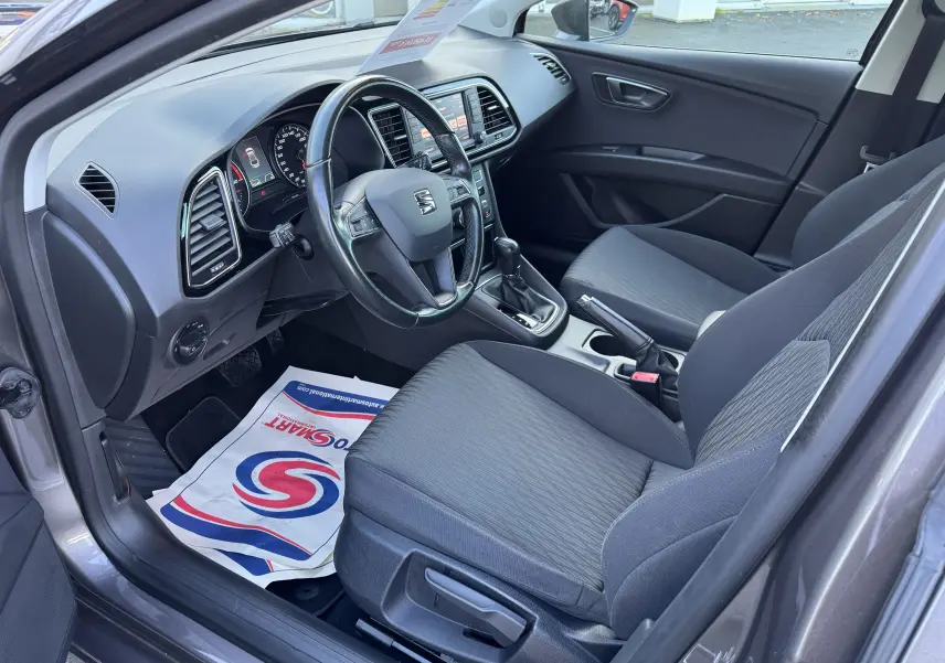 Intérieur avant droit d'une SEAT Leon gris 2016, montrant le tableau de bord, volant cuir et sièges tissu noirs.