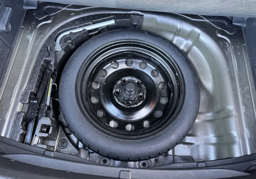 Vue plongeante sur la roue de secours noire et les outils de bord dans le coffre d'un SEAT Leon gris 2016.