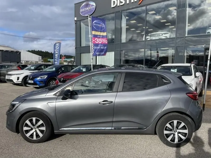 Profil côté gauche d'une Renault Clio V gris foncé métal 2023, avec jantes alliage et vitres teintées, devant un concessionnaire.