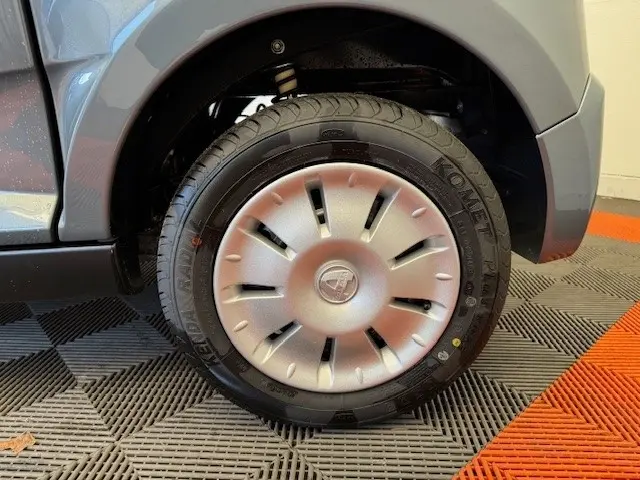 Gros plan sur la roue avant droite d’une Aixam Ambition 0.5 City Pack gris foncé, avec jante et logo central visibles.