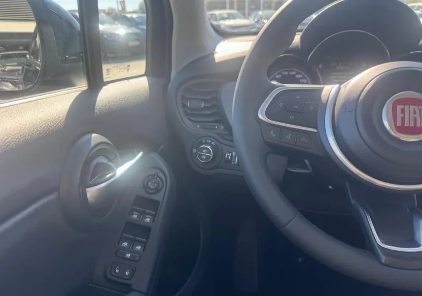 Vue intérieure côté gauche du volant du Fiat 500X bleu, montrant commandes de vitres et volant avec logo FIAT.