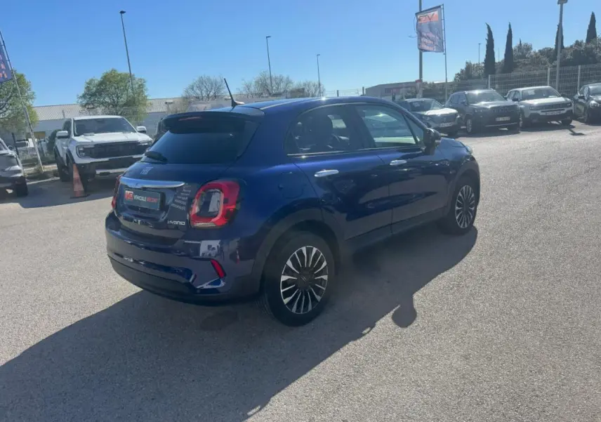 Fiat 500X bleu en 3/4 arrière droit sur parking, avec jantes classiques 16 pouces et feux arrière distinctifs.