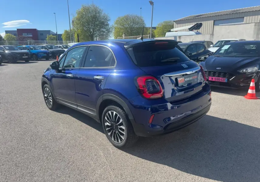 Vue 3/4 arrière droite d'une FIAT 500X bleu métallisé avec jantes classiques 16 pouces sur parking extérieur.