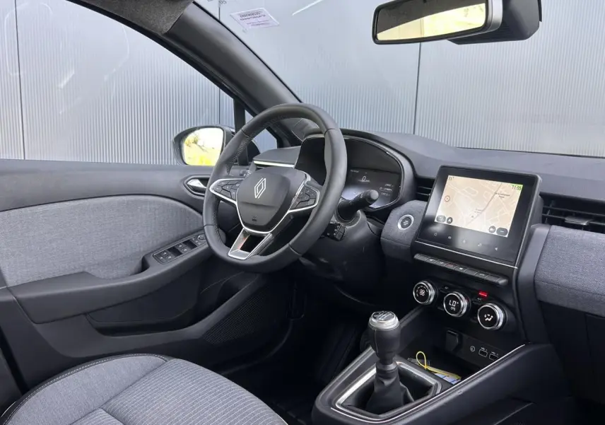 Vue intérieure côté conducteur de la Renault Clio 2025, volant multifonction, écran tactile et levier de vitesses manuel.