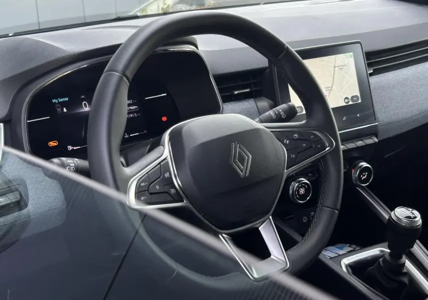 Intérieur de Renault Clio 2025, vue centrée sur le volant multifonction noir et la console avec écran tactile.