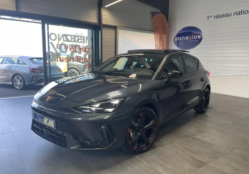 Vue 3/4 avant d'une CUPRA Leon gris magnétique avec jantes cuivrées et toit ouvrant panoramique en showroom.