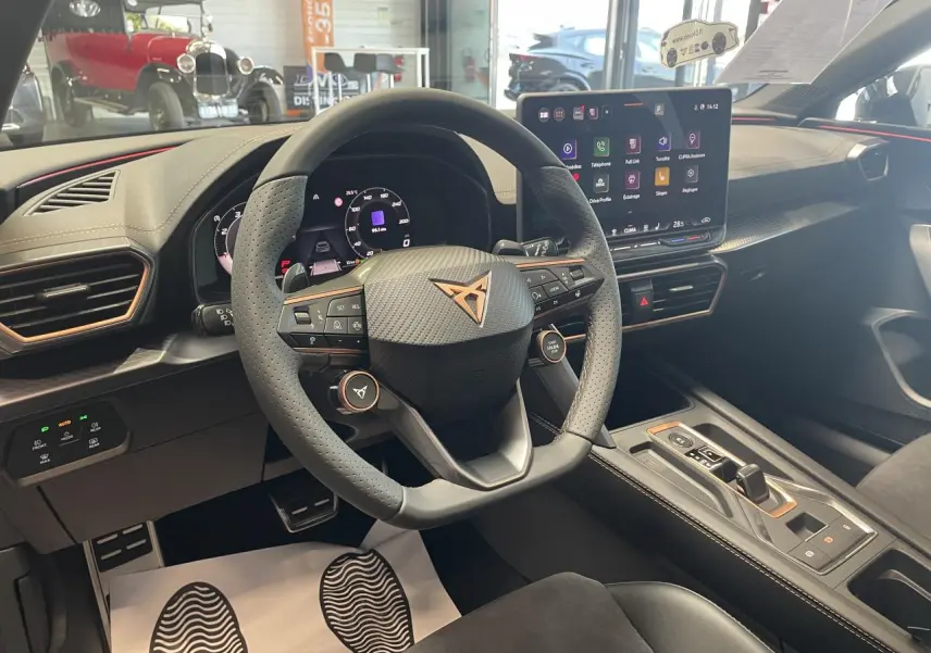 Vue intérieure du poste de conduite du CUPRA Leon gris, volant perforé avec logo cuivré et écran tactile central lumineux.