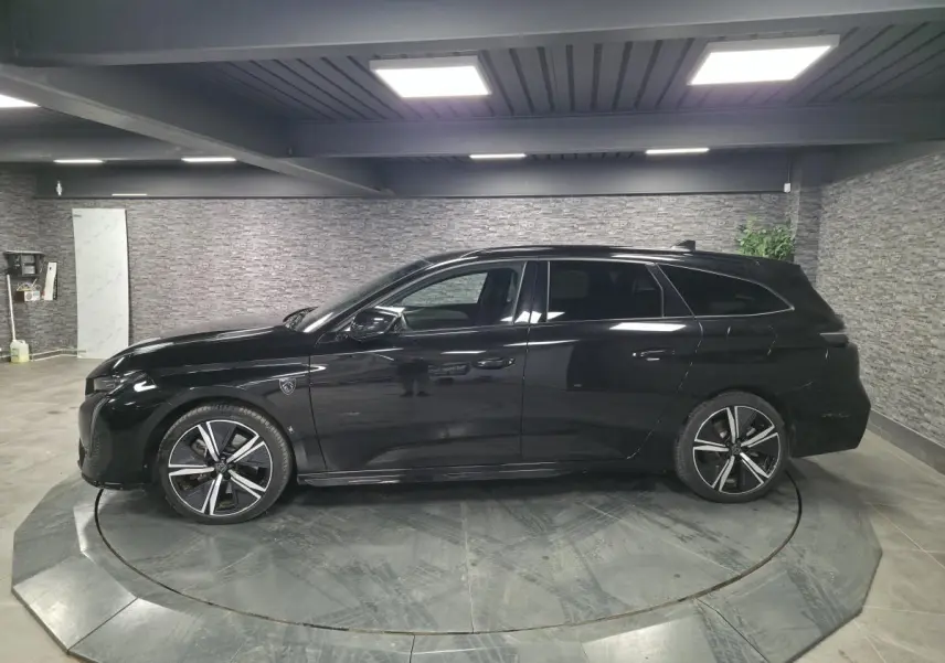 Peugeot 308 SW GT noire vue de profil côté gauche, jantes alliage 18'' et toit noir brillant en intérieur showroom.