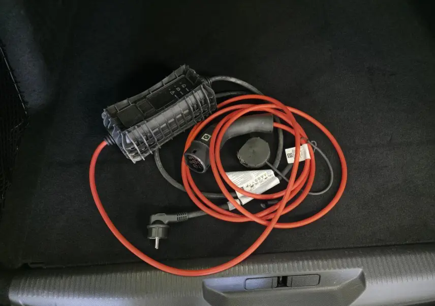 Câble de recharge hybride rouge et noir dans le coffre d'une Peugeot 308 SW noire, vue intérieure du coffre.