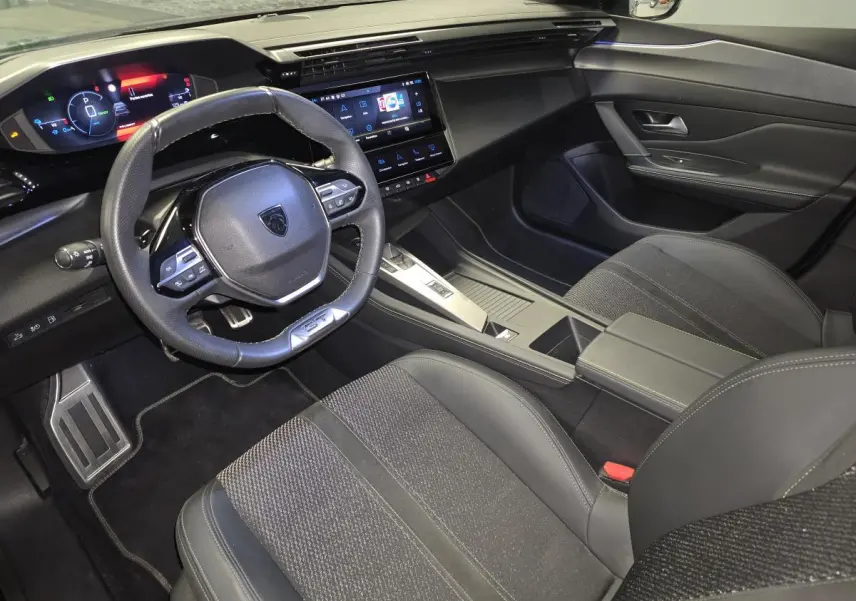 Vue intérieure côté conducteur de la Peugeot 308 SW GT 2024 noire, avec volant cuir, écran tactile et sellerie tri-matières.
