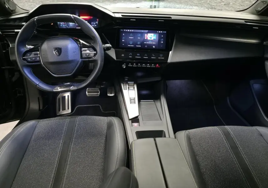 Vue intérieure avant de la Peugeot 308 SW GT 2024 noire, avec volant cuir, écran tactile central et sièges tissu/TEP.