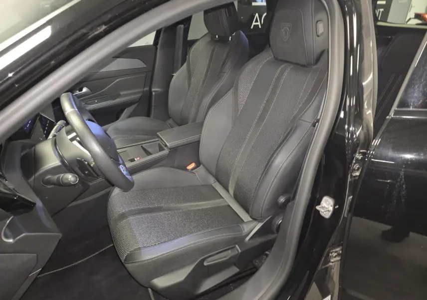 Vue intérieure côté conducteur de la Peugeot 308 SW 2024 noire, sièges tissu/TEP avec logo Peugeot brodé sur appuie-tête.