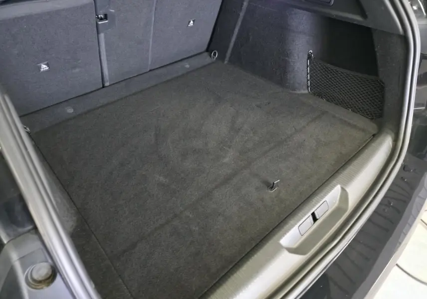 Vue intérieure du coffre arrière noir du Peugeot 308 SW 1.6 PHEV 2024, avec tapis et filet de rangement latéral.