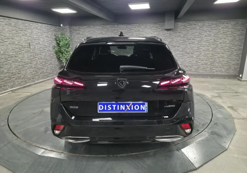 Vue arrière d'une Peugeot 308 SW hybride noire avec feux arrière LED allumés dans un showroom.