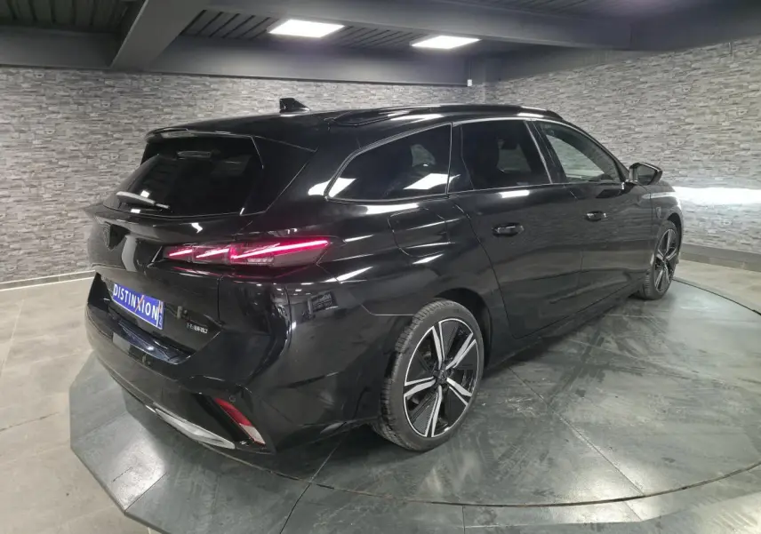 Peugeot 308 SW hybride noire vue en 3/4 arrière droit, feux arrière LED allumés et jantes alliage 18 pouces.