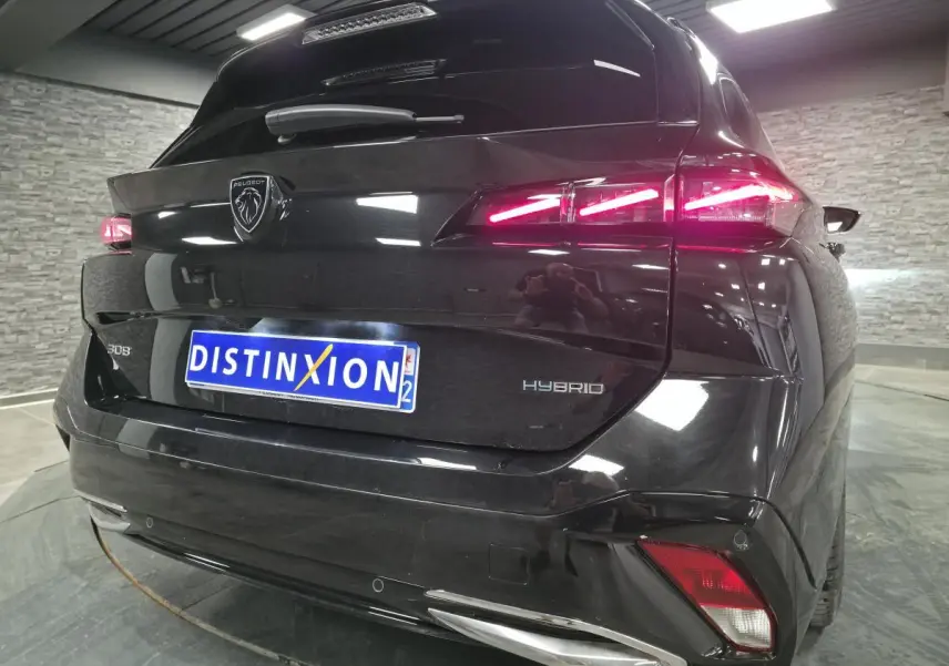 Vue 3/4 arrière d'une Peugeot 308 SW hybride noire avec feux arrière LED allumés et logo lion chromé.