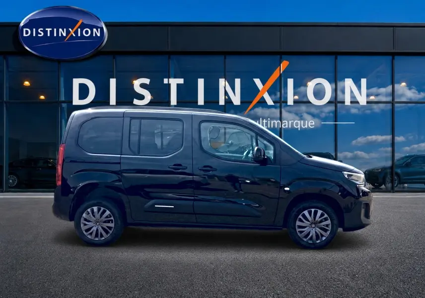 Profil droit du Citroën Berlingo noir 2026, avec barres de toit et jantes alliage visibles devant une vitrine Distinxion.