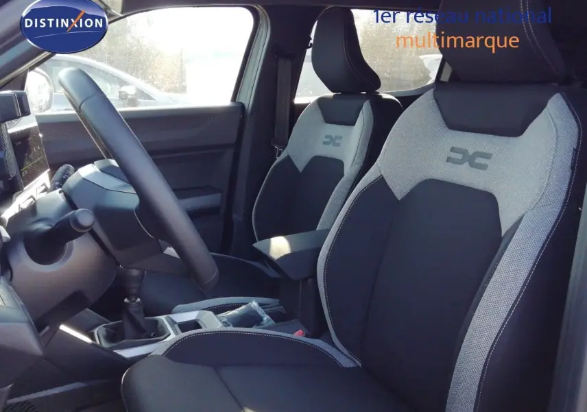 Vue intérieure côté conducteur du Dacia Duster 2026, montrant les sièges bi-ton gris et noir avec logo DC brodé.