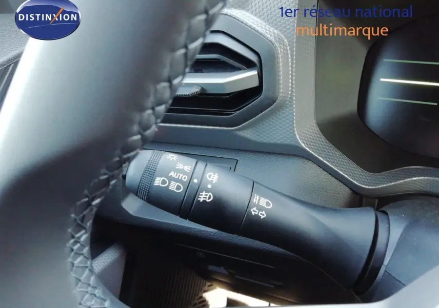Gros plan sur la commande des feux à gauche du volant d’un Dacia Duster gris schiste métal, intérieur noir.