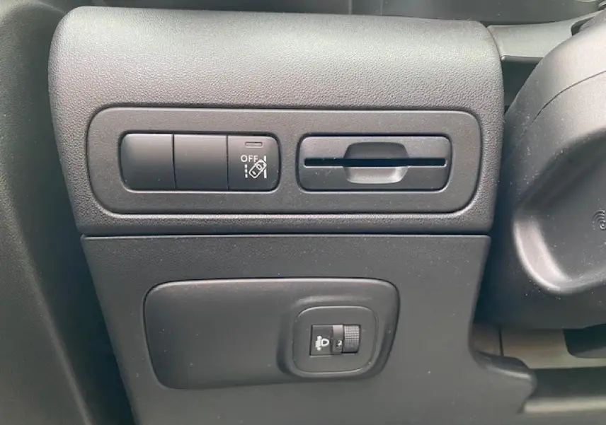 Vue rapprochée des commandes de réglage des phares et des aides à la conduite sur le tableau de bord noir du Citroën C3 Aircross.
