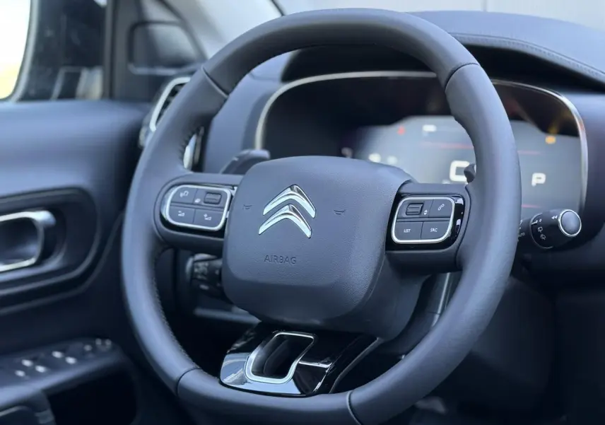 Gros plan sur le volant cuir noir du Citroën C5 Aircross 2025 avec commandes intégrées et logo chromé central.