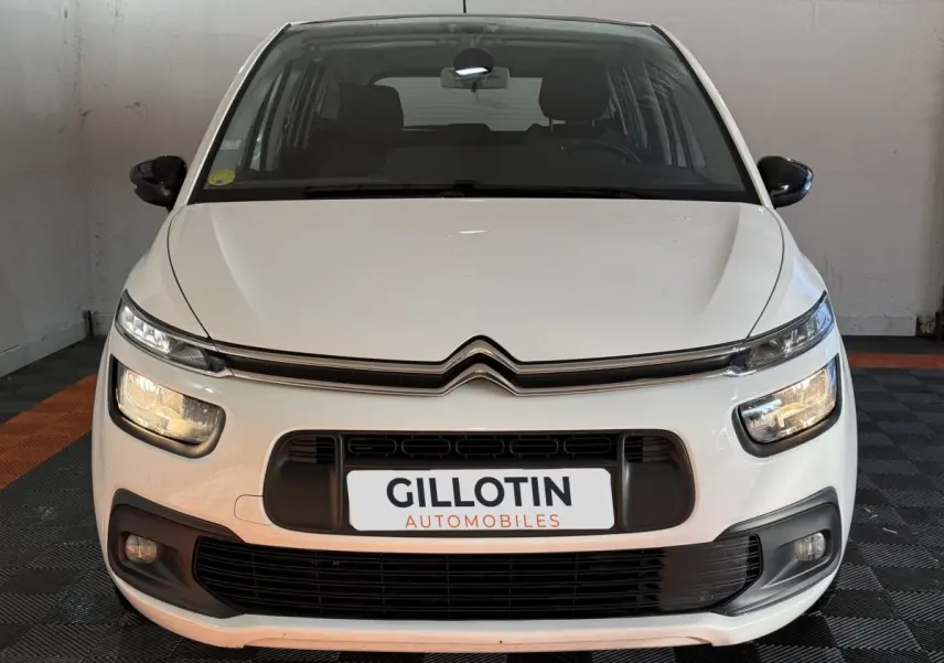 Vue frontale d'un Citroën Grand C4 Spacetourer blanc avec phares allumés dans un garage.