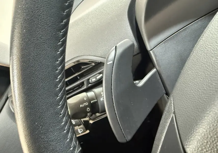 Gros plan sur la palette de changement de vitesse noire derrière le volant cuir noir du Citroën Grand C4 Spacetourer blanc.