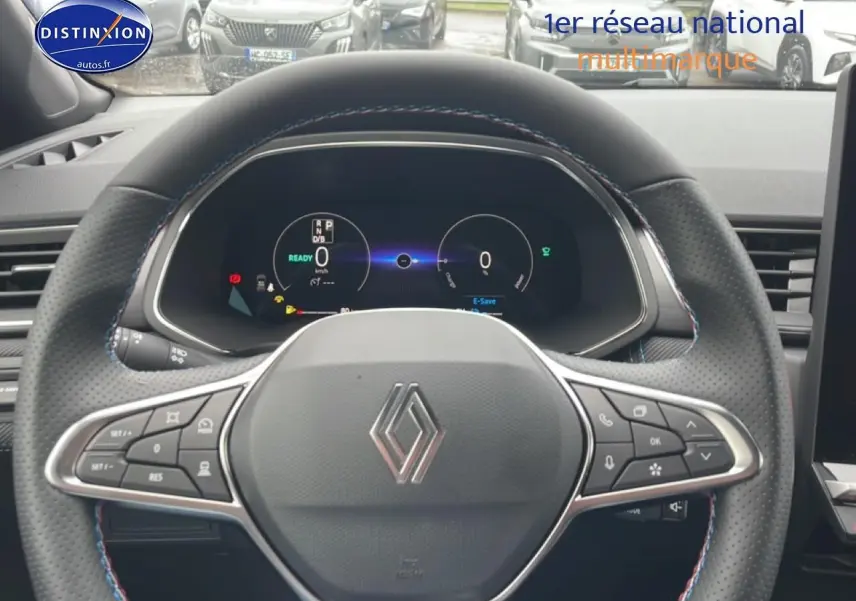 Vue rapprochée du volant cuir perforé avec logo Renault et tableau de bord numérique du Captur gris cassiopée 2025.