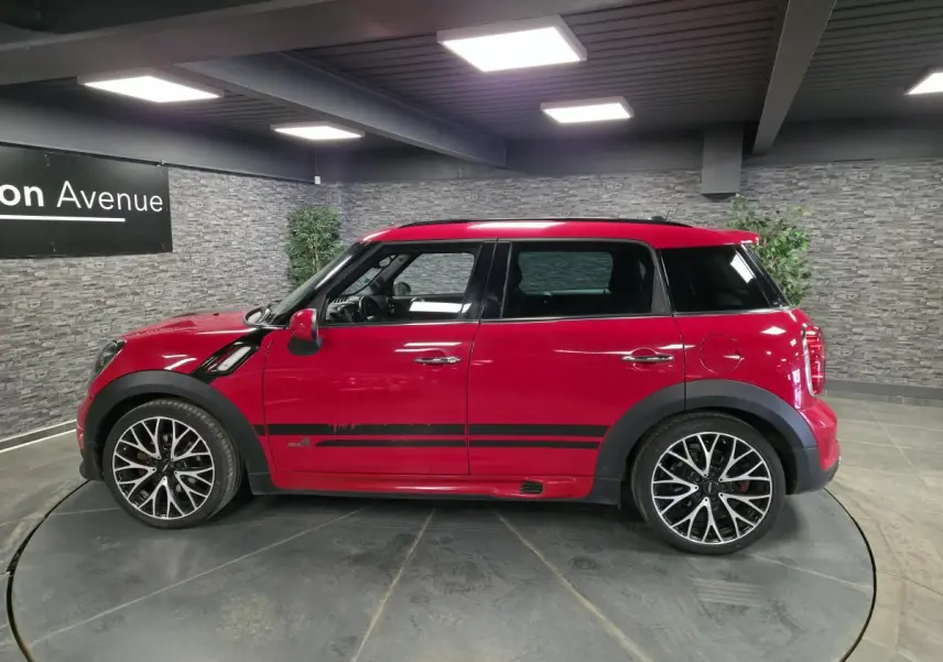 Profil droit d'une MINI Countryman John Cooper Works rouge avec bandes sport noires et jantes alliage distinctives.
