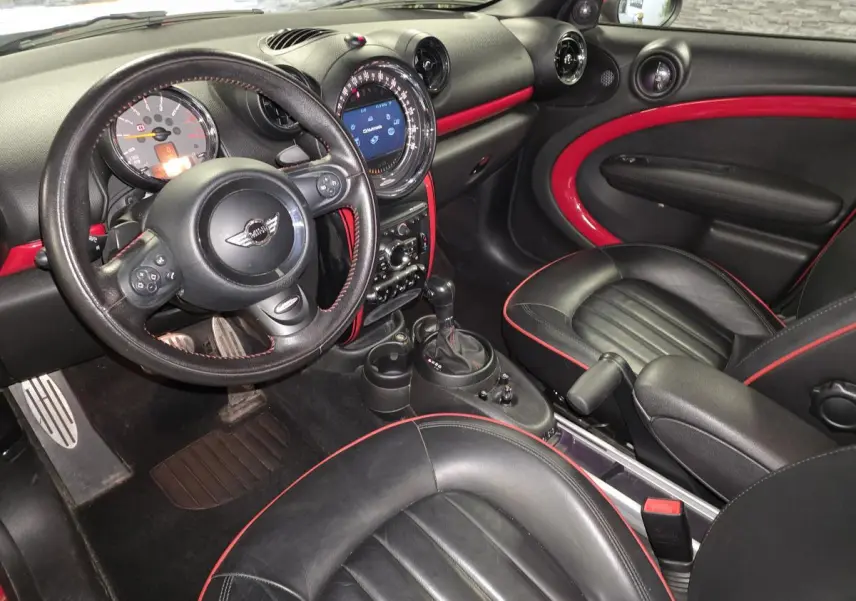 Vue intérieure côté conducteur de la MINI Countryman John Cooper Works 2015, cuir noir avec surpiqûres rouges et inserts rouges sur tableau de bord.