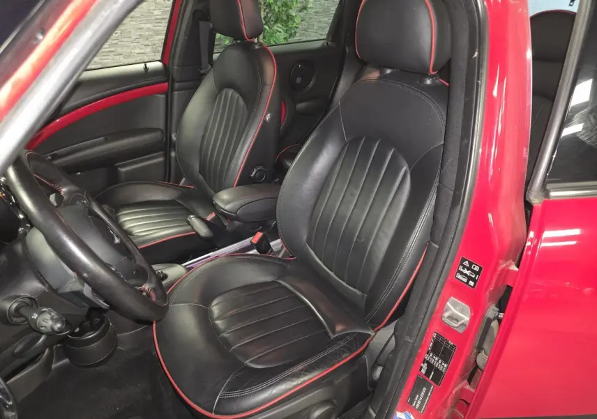 Vue intérieure côté conducteur d'une MINI Countryman John Cooper Works 2015 rouge, sièges cuir noirs avec surpiqûres rouges.
