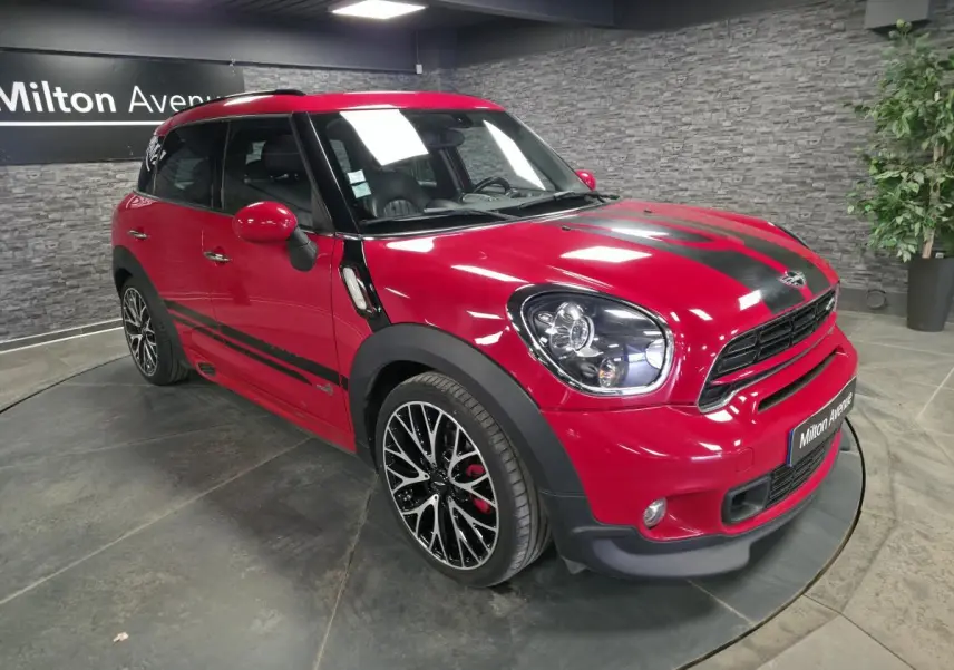 Vue 3/4 avant droite d'une MINI Countryman John Cooper Works rouge avec bandes noires sport et jantes noires à dessin complexe.