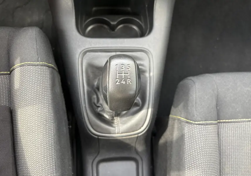 Vue plongeante sur le levier de vitesses manuel noir d’une Citroën C3 blanche, entouré des sièges gris à surpiqûres jaunes.