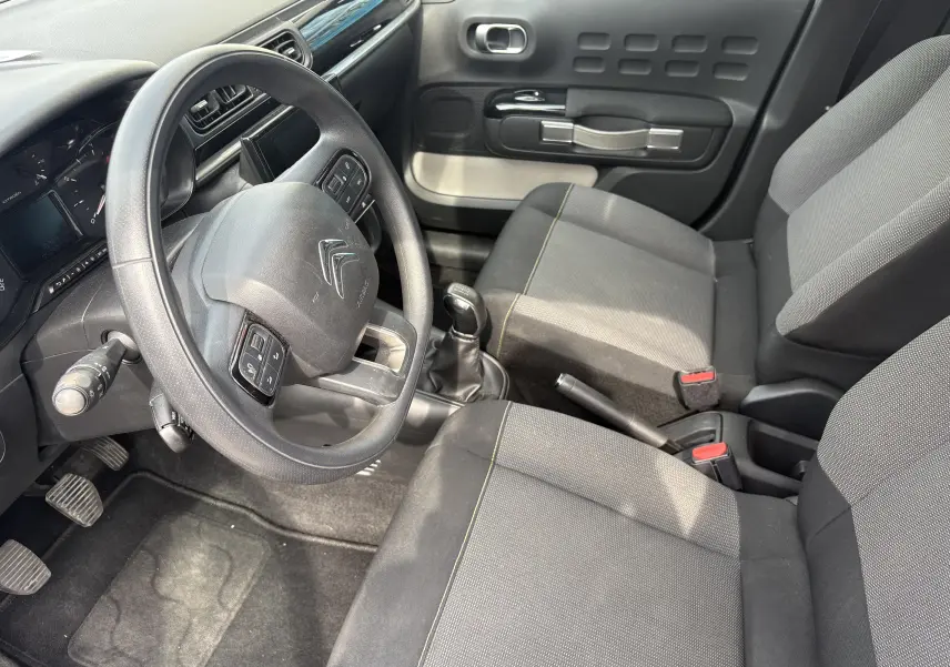 Vue intérieure côté conducteur de la Citroën C3 blanche 2019, volant multifonction et sièges tissu gris.