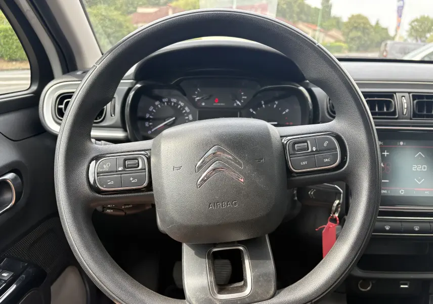 Vue rapprochée du volant noir de la Citroën C3 blanche 2019, avec commandes intégrées et tableau de bord en arrière-plan.