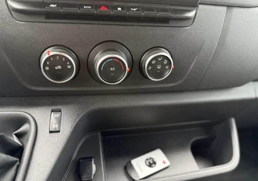 Gros plan sur les commandes de climatisation et la console centrale noire du Nissan NV400 Fourgon blanc 2020.