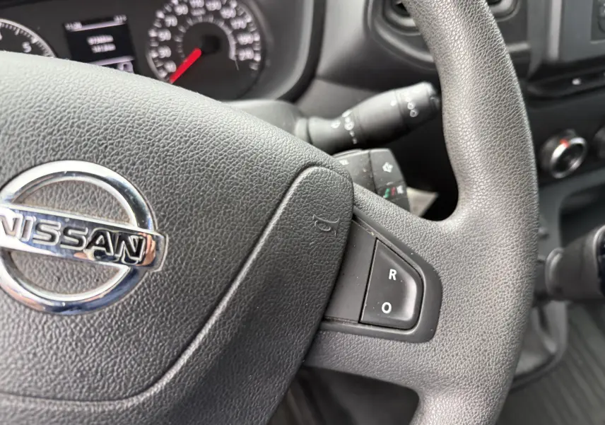 Gros plan sur le volant noir du Nissan NV400 Fourgon 2020 avec commandes intégrées et tableau de bord en arrière-plan.