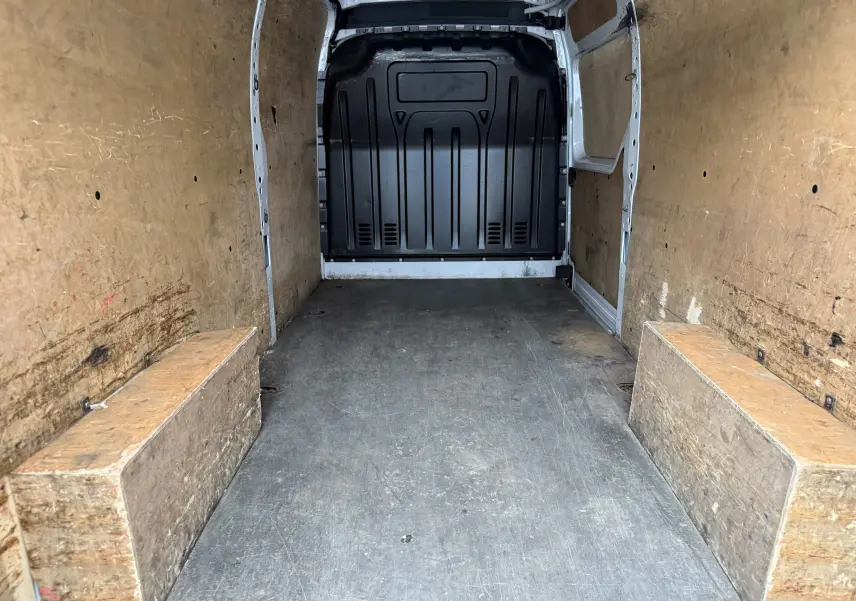 Intérieur du fourgon Nissan NV400 blanc vu de l'arrière, montrant la zone de chargement avec parois et protections en bois.