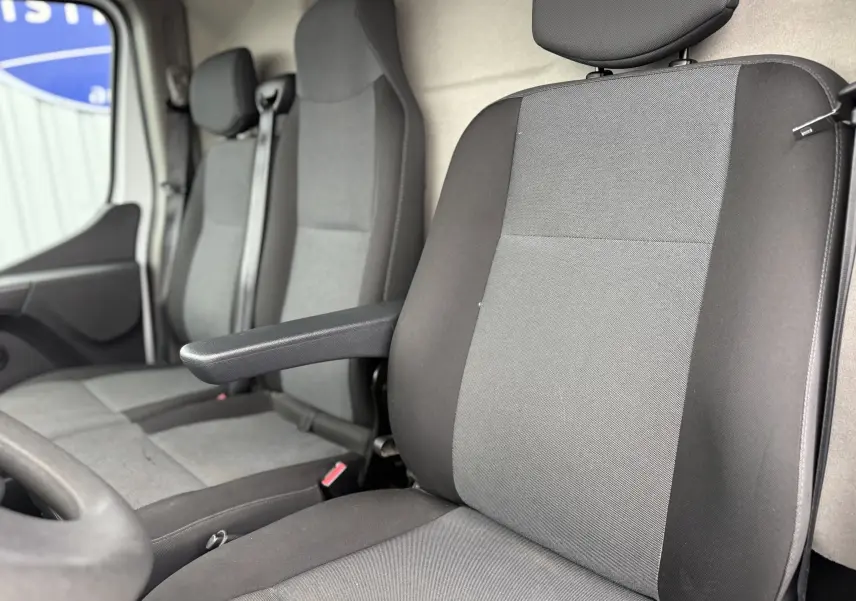 Gros plan sur les sièges avant gris et noirs du Nissan NV400 Fourgon blanc, version 2020, avec accoudoir côté conducteur.