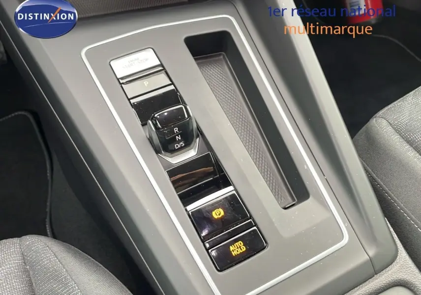 Gros plan sur la console centrale avec levier de vitesse automatique et boutons de frein à main et maintien auto sur Volkswagen Golf VIII.