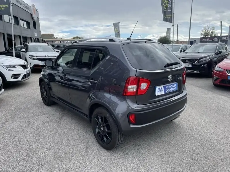 Suzuki Ignis gris foncé métal vue 3/4 arrière droit avec jantes noires et toit équipé de barres de toit.
