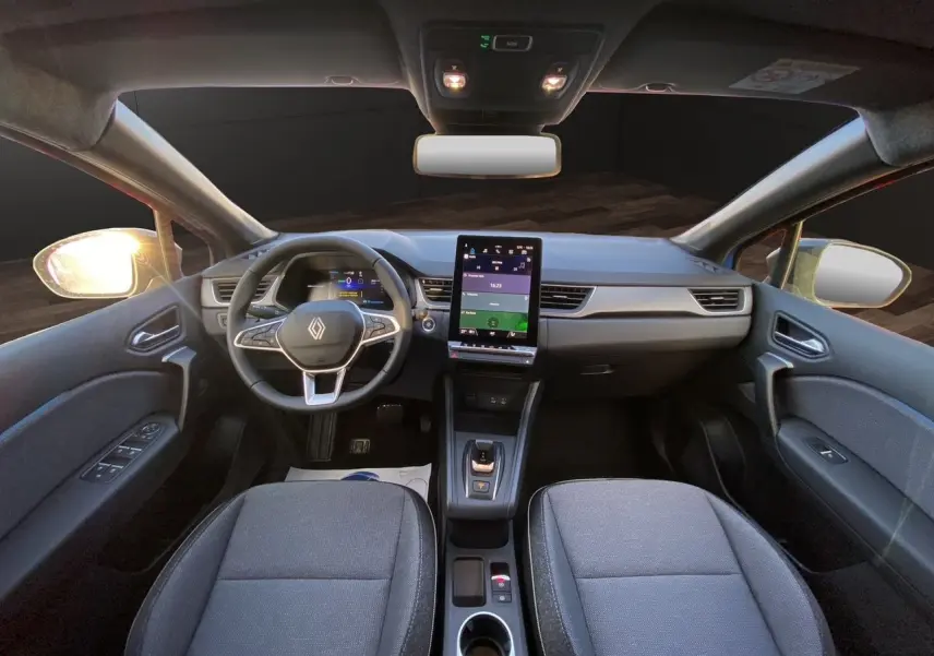 Vue intérieure avant du Renault Captur 2025, tableau de bord moderne avec écran tactile vertical et sièges gris foncé.
